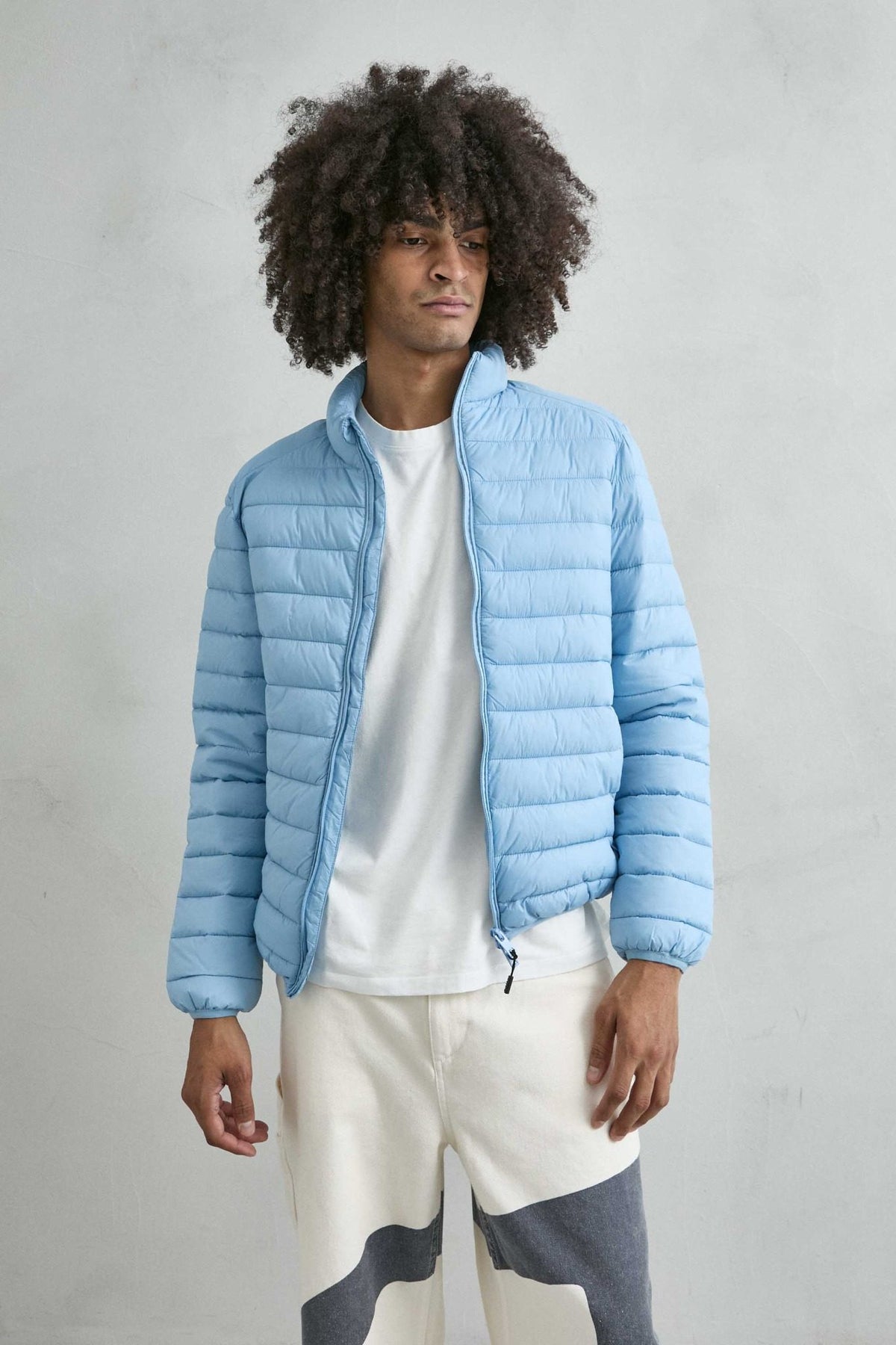 Chaqueta acolchada de hombre azul cielo con cuello alto y cremallera de doble cursor, vista frontal.