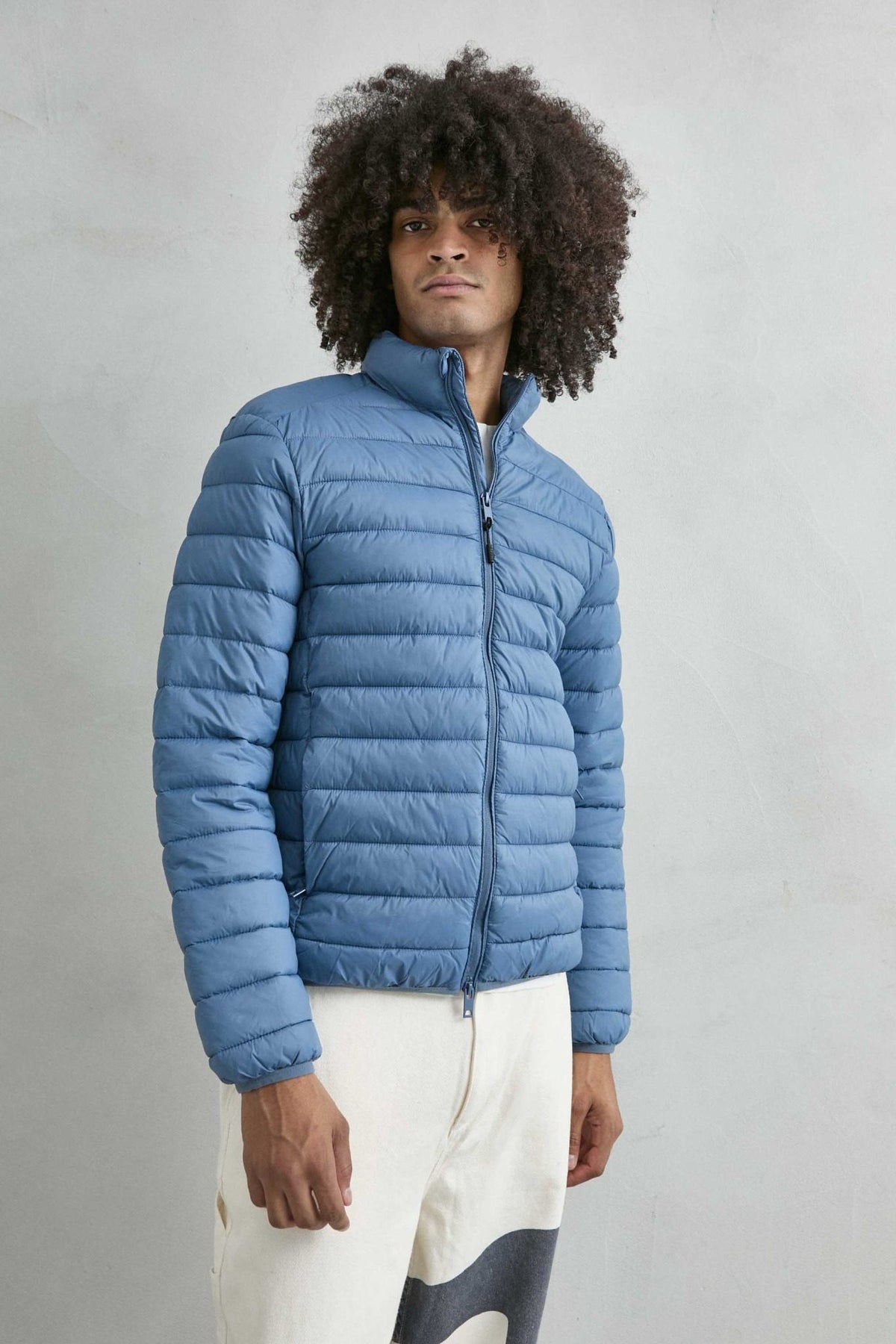 Chaqueta acolchada de hombre azul claro con cuello alto y cremallera de doble cursor, vista frontal.