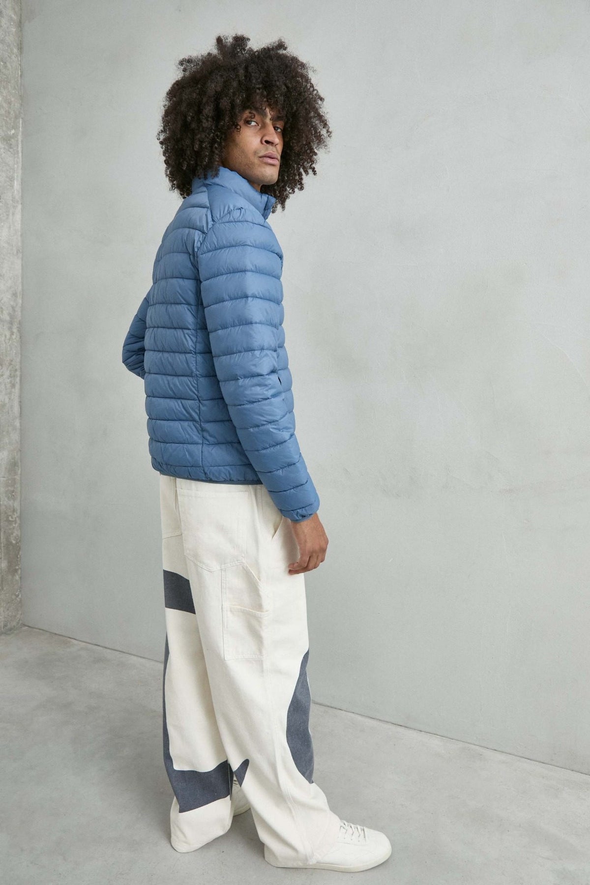 Chaqueta acolchada de hombre azul claro con cuello alto y cremallera de doble cursor, vista lateral.