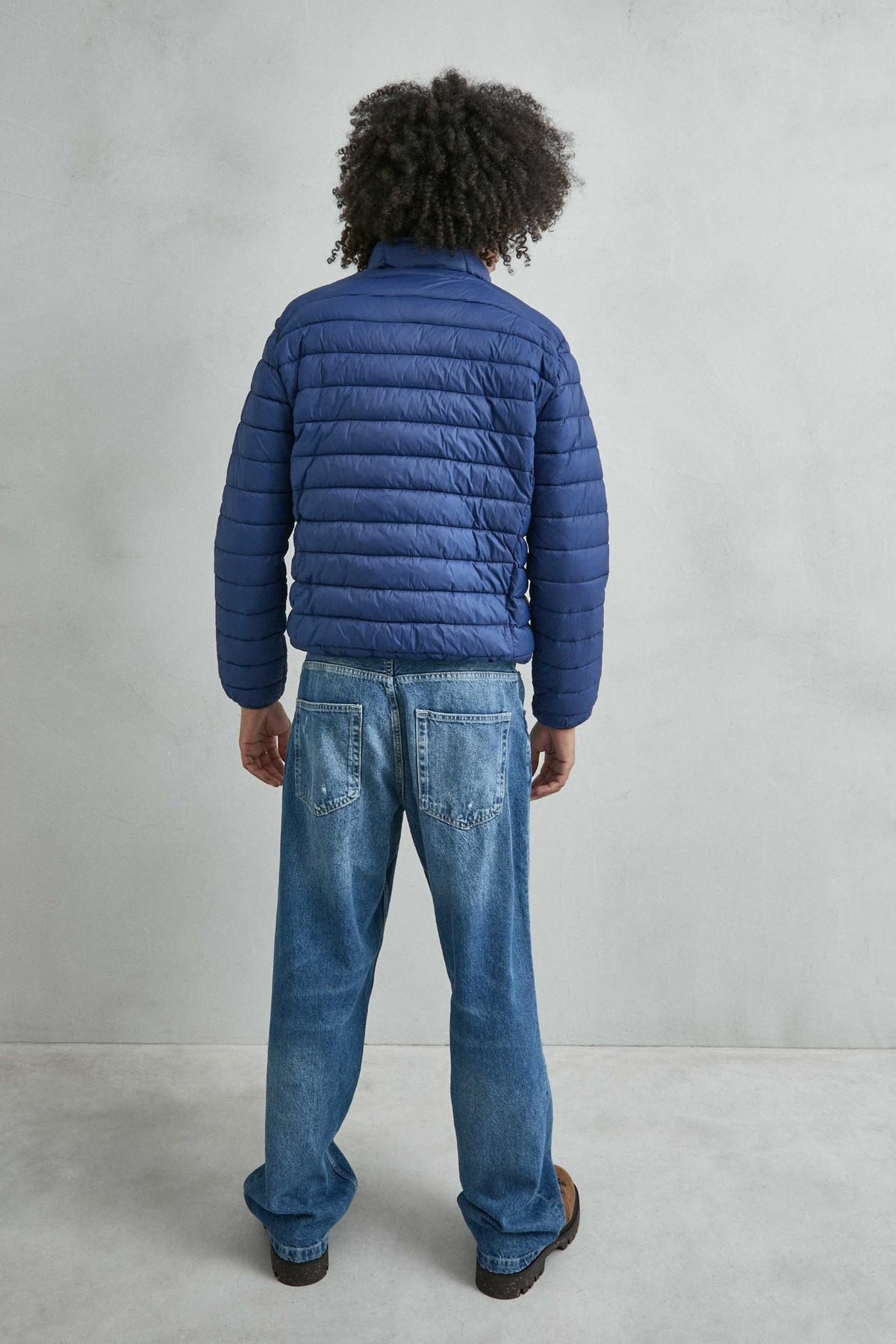 Chaqueta acolchada de hombre azul con cuello alto y cremallera de doble cursor, vista espalda.