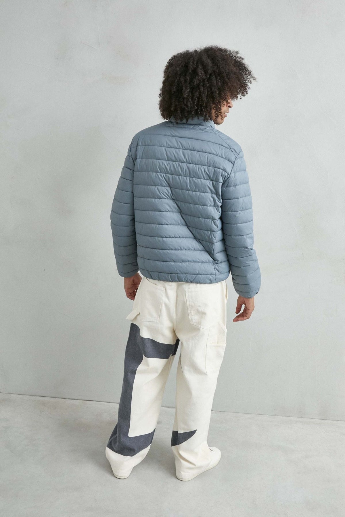 Chaqueta acolchada de hombre azul grisáceo con cuello alto y cremallera de doble cursor, vista espalda.