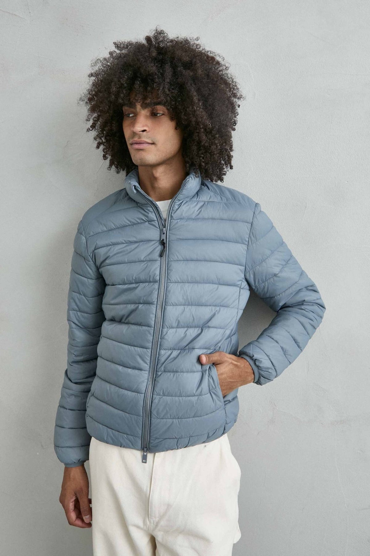 Chaqueta acolchada de hombre azul grisáceo con cuello alto y cremallera de doble cursor, vista frontal.