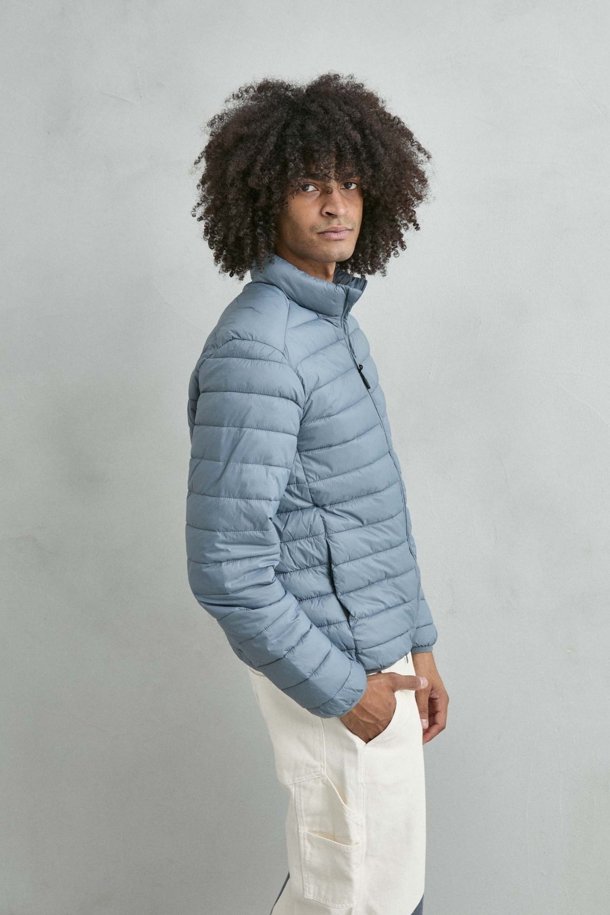 Chaqueta acolchada de hombre azul grisáceo con cuello alto y cremallera de doble cursor, vista lateral.