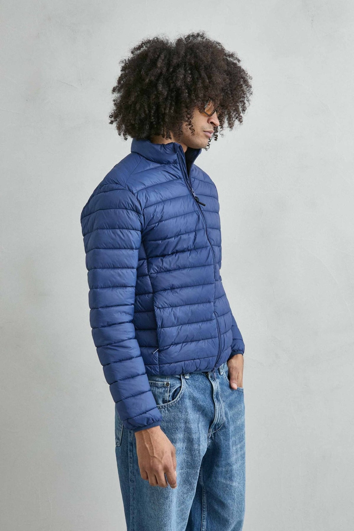 Chaqueta acolchada de hombre azul con cuello alto y cremallera de doble cursor, vista lateral.