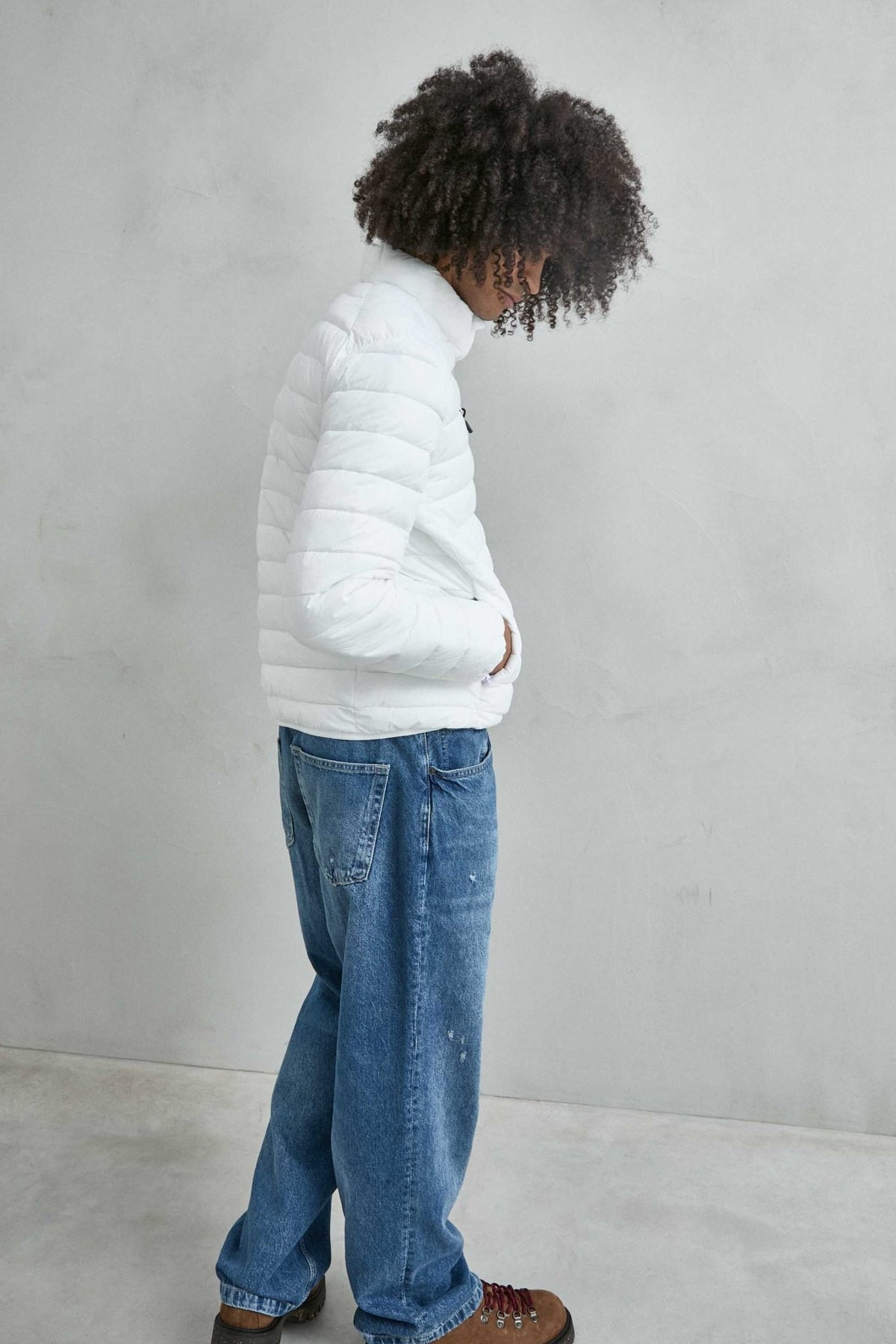Chaqueta acolchada de hombre blanco con cuello alto y cremallera de doble cursor, vista lateral.