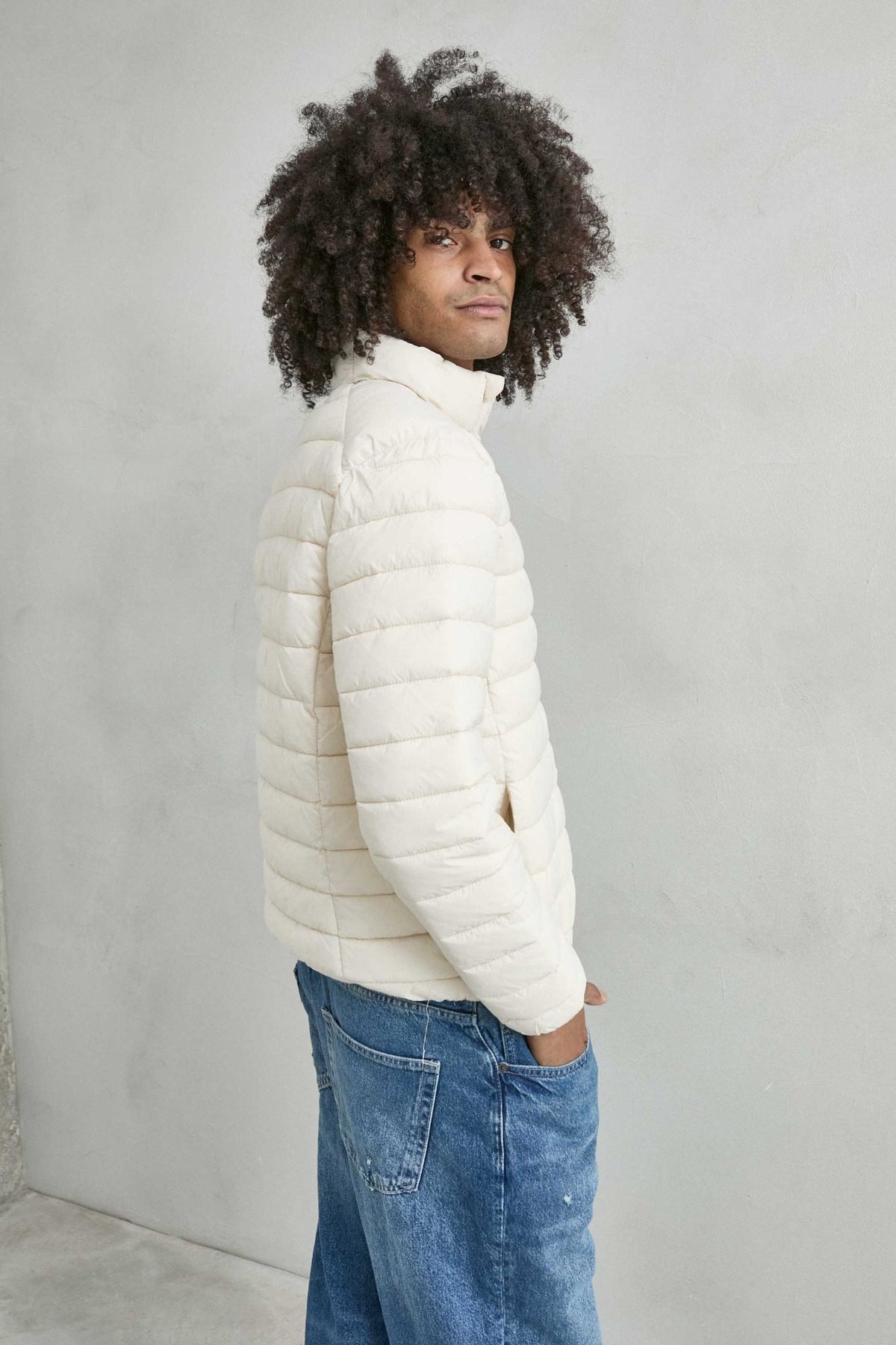 Chaqueta acolchada de hombre crema con cuello alto y cremallera de doble cursor, vista lateral.