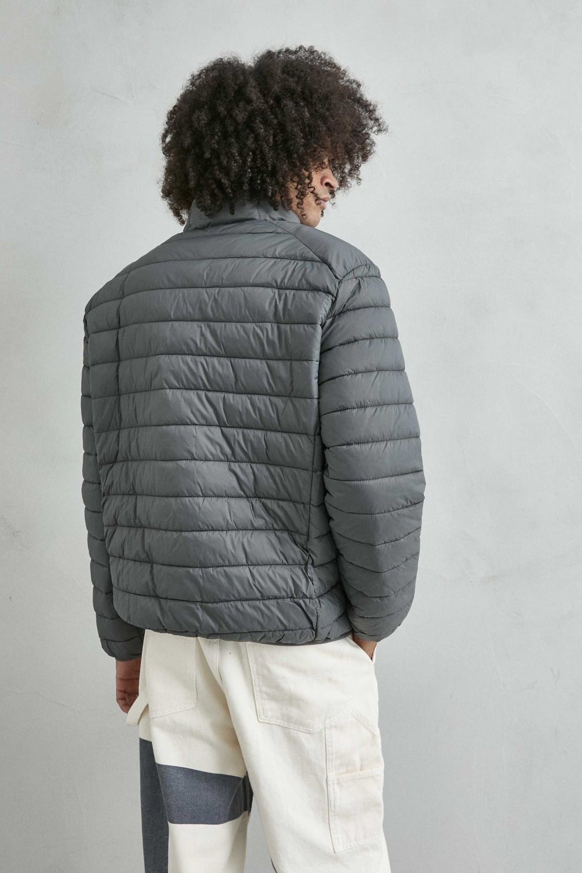 Chaqueta acolchada de hombre gris con cuello alto y cremallera de doble cursor, vista espalda.