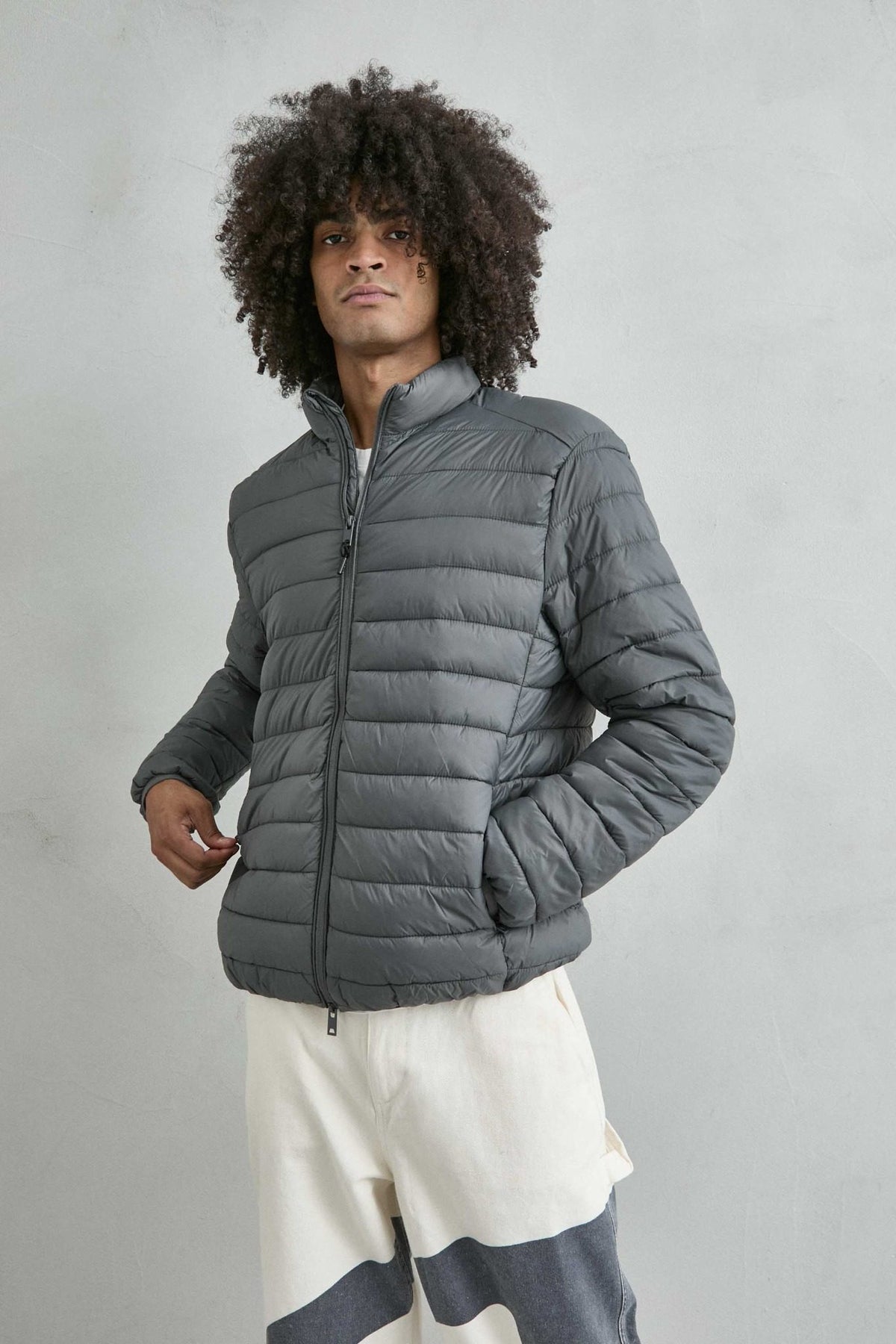 Chaqueta acolchada de hombre gris con cuello alto y cremallera de doble cursor, vista frontal.