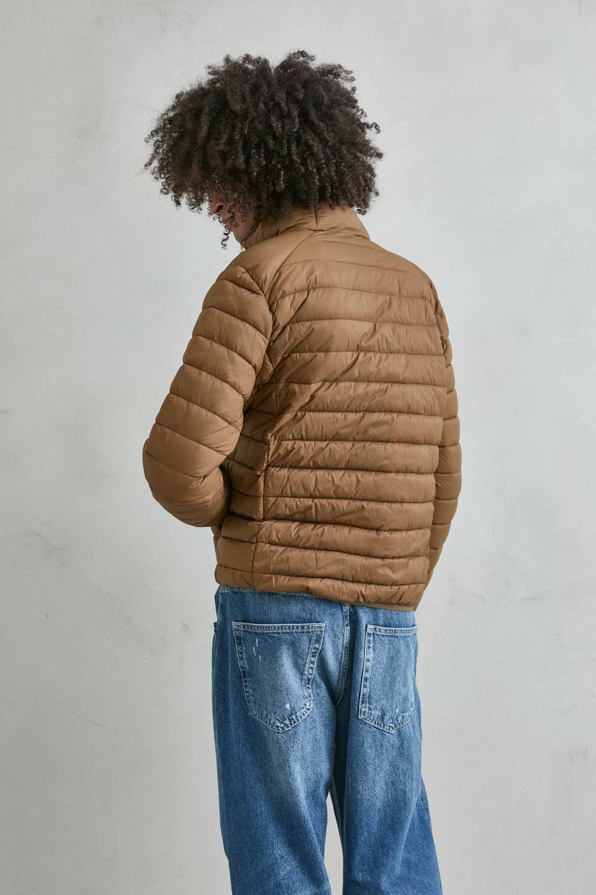 Chaqueta acolchada de hombre marrón con cuello alto y cremallera de doble cursor, vista lateral.