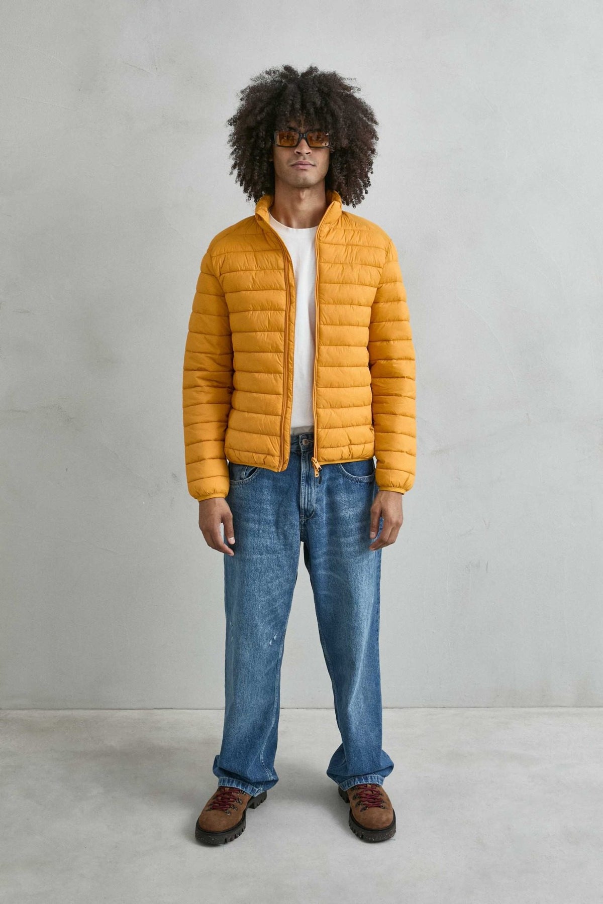Chaqueta acolchada de hombre mostaza con cuello alto y cremallera de doble cursor, vista de cuerpo entero.