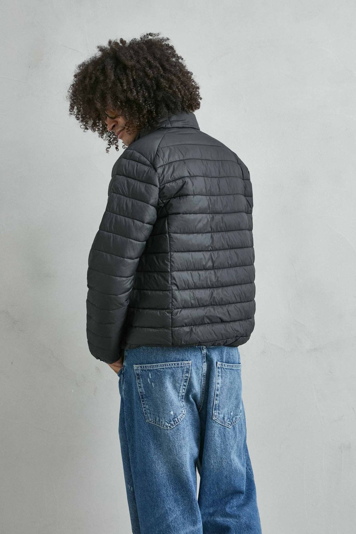 Chaqueta acolchada de hombre negro con cuello alto y cremallera de doble cursor, vista espalda.