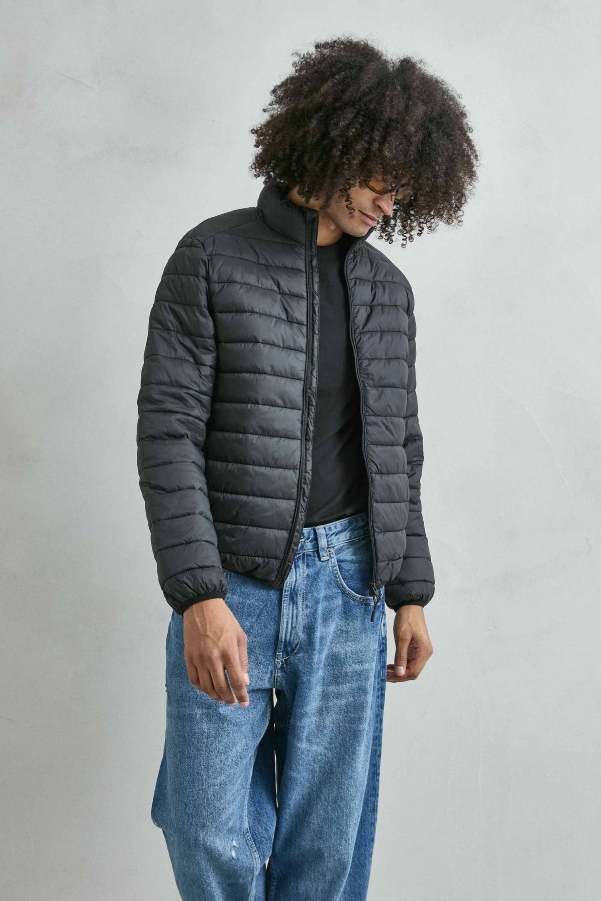 Chaqueta acolchada de hombre negro con cuello alto y cremallera de doble cursor, vista frontal.
