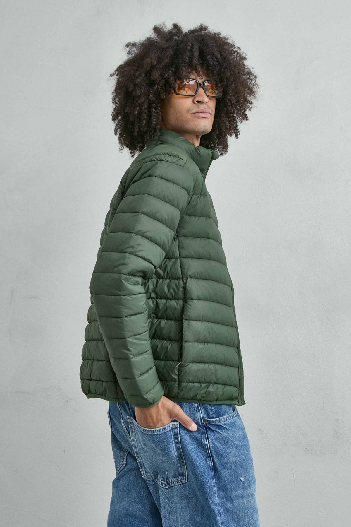 Chaqueta acolchada de hombre verde militar con cuello alto y cremallera de doble cursor, vista lateral.