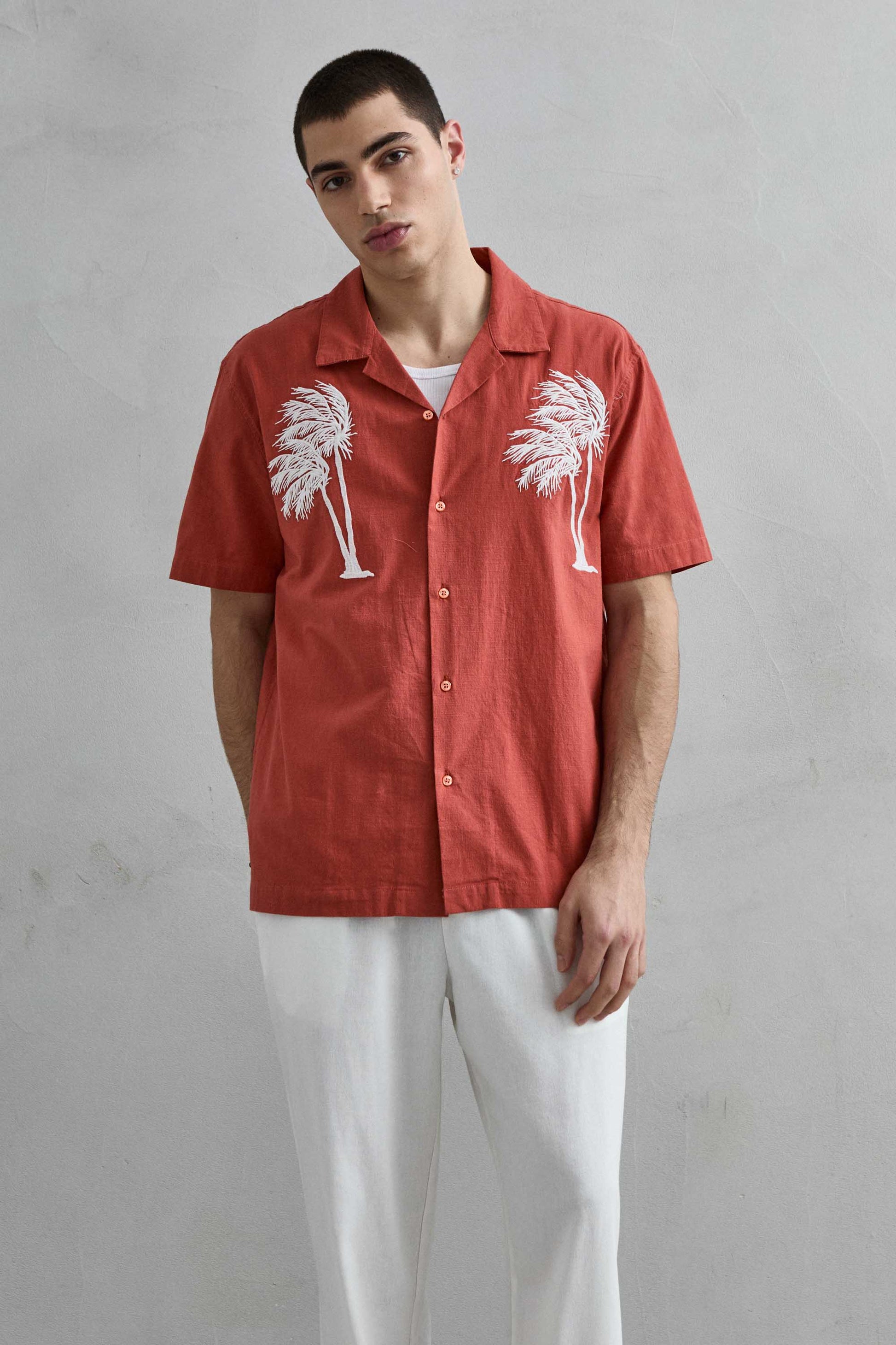 Camisa de manga corta en color terracota de Imperio con cuello cubano y bordado de palmeras blancas, vista frontal.