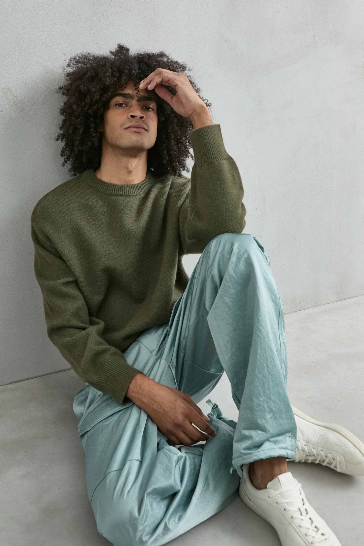Modelo sentado con jersey liso oversize de hombre en verde oliva