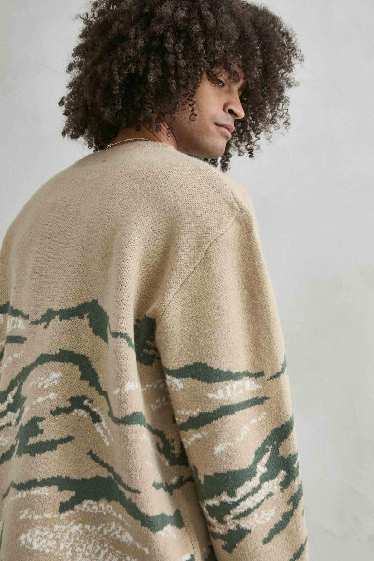 Detalle del punto y del hombro en la espalda del jersey oversize con paisaje de montañas en arena y verde