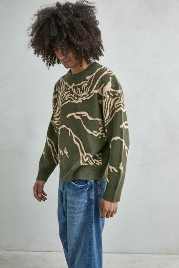 Vista frontal de medio cuerpo del jersey oversize verde oliva con dibujo abstracto en beis