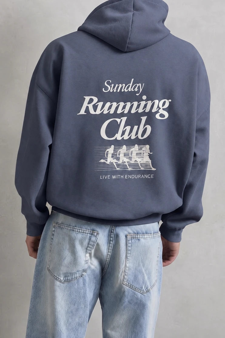 Espalda de sudadera azul con texto Sunday Running Club y siluetas blancas de corredores