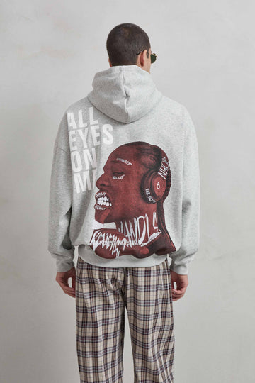 Vista trasera de sudadera gris jaspe con gráfico “ALL EYES ON ME” y rostro expresivo