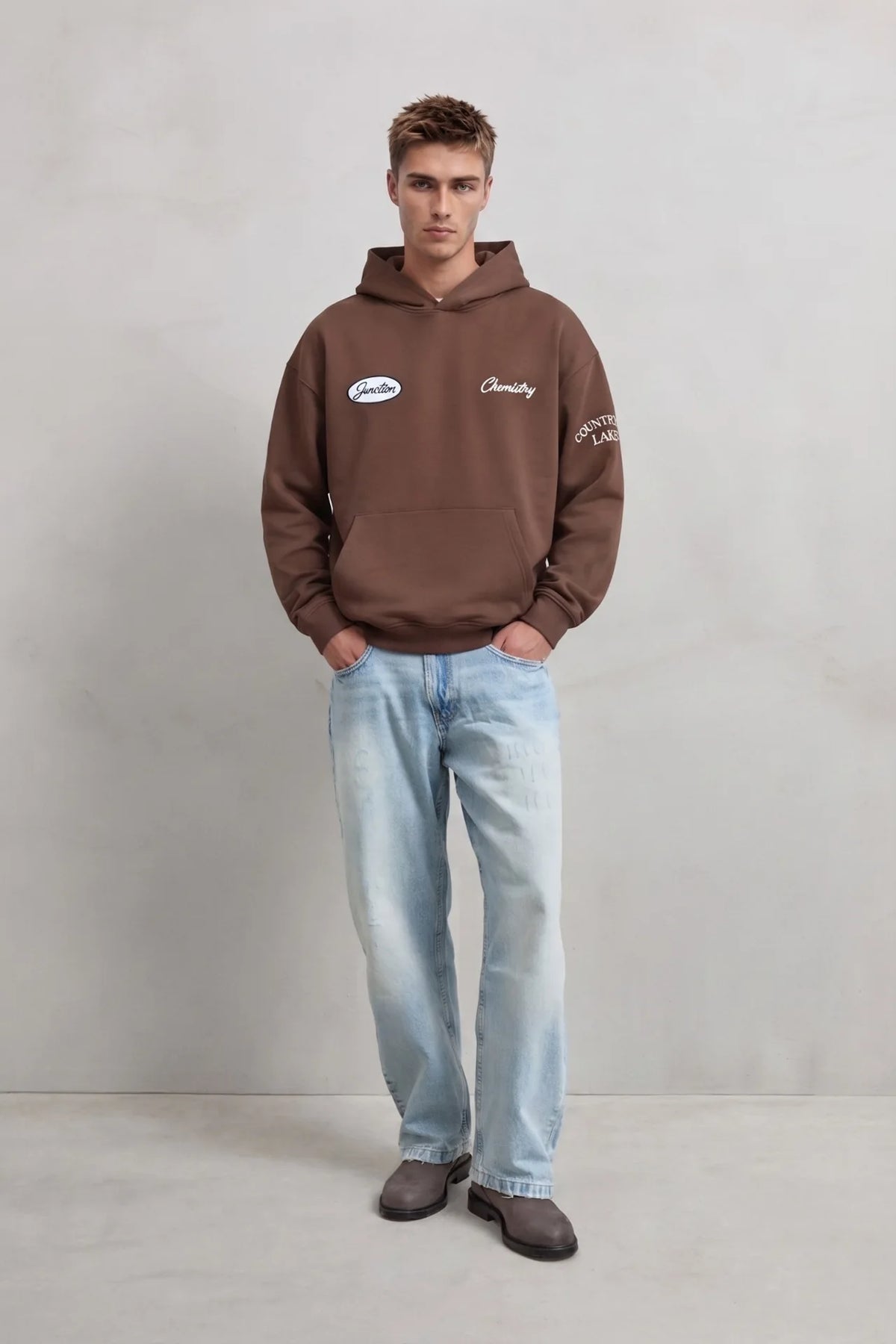 Vista frontal de cuerpo entero con sudadera marrón Chemistry con letras en la manga y vaqueros claros