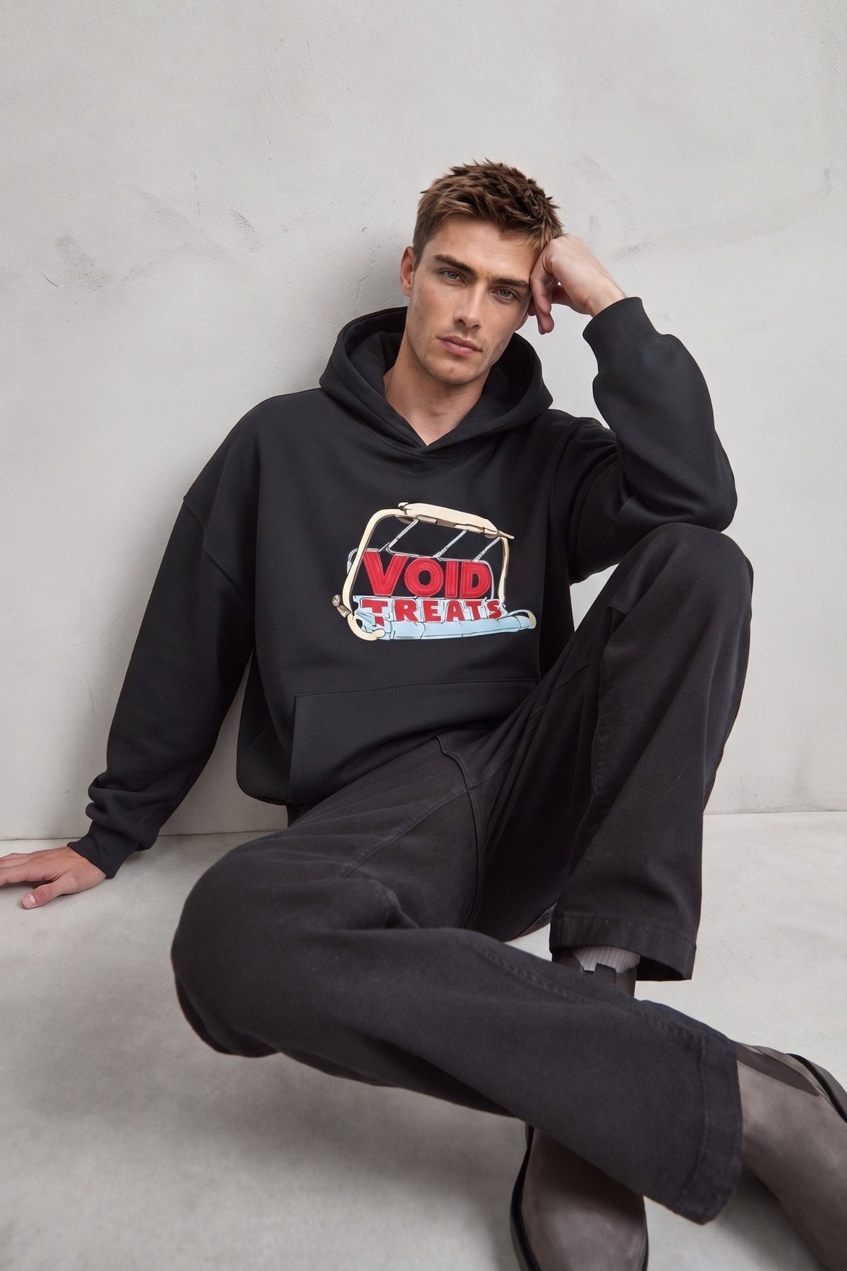 Sudadera negra oversize con capucha y estampado frontal, modelo sentado
